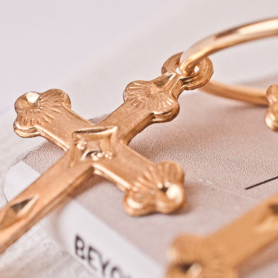 Etched cross suspended from a gold hoop earrings