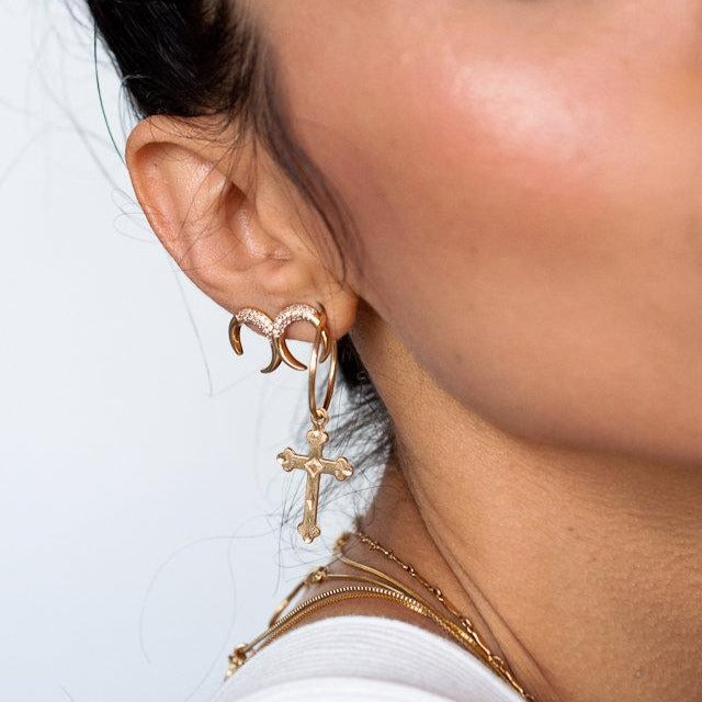 Women wearing layering chain necklaces with cross hoop earrings and double horn stud earrings, she is wearing a white tank top as well.