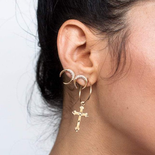 Cross hoop earrings gold on women, she is also wearing double horn earrings on a stacked earring look